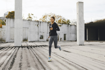 Young fit woman running in the industrial urban zone, side view of fitness girl running