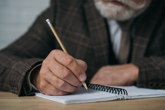 close-up shot of senior man writing in notebook with pencil