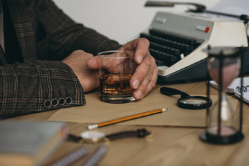 cropped shot of senior writer with glass of whiskey at workplace