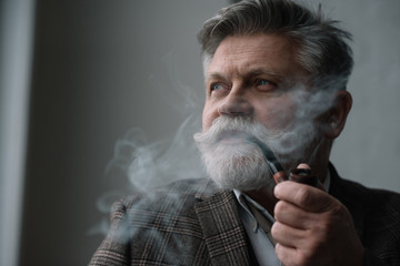 close-up portrait of bearded senior man smoking pipe