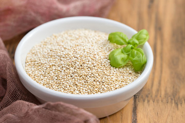 uncooked quinoa in white bowl on brown wooden background
