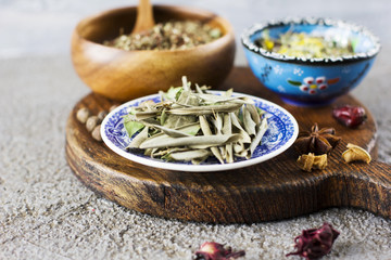 Dried olive leaves and dry spices in bowls on wooden Board on a concrete background