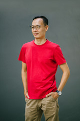 Fototapeta premium Portrait of a young Asian man leaning against a gray wall while smiling and posing in front of the camera. He seems reliable, confident and relaxed 