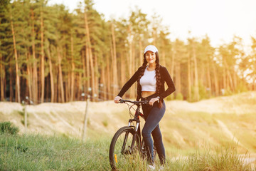 Beautiful young woman riding bicycle at the forest. Stylish young female cycling on an evening spring promenade on a hot day.