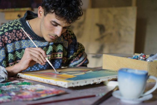 Male artist painting canvas in artists studio, cropped