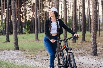 Fototapeta na wymiar Perfect day for cycling. Low angle view of young girl riding bicycle along a road. Woman outdoors in nice spring park, wearing jacket and trendy sports outfit, sneakers, smiling