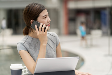 Young city businesswoman making smartphone call from sidewalk cafe