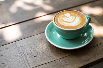 a cup of cappuccino with latte art on wooden background. Beautiful foam, greenery ceramic cups, stylish toning, place for text.