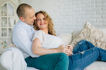 Fototapeta na wymiar Expecting couple lying on couch in living room. Happy pregnancy concept