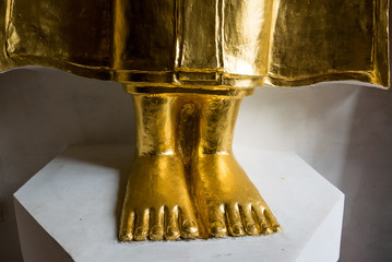 Close focus on feet of golden Buddha statue on white stand. Gold foot of Buddha statue. Religion and Travel in Thailand.