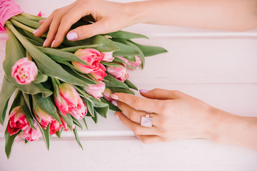 A bouquet of red tulips which a girl hugs her hands on a pink background