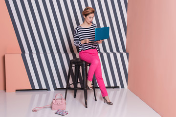 Stylish woman with a laptop in her hands in a striped T-shirt and pink pants, lifestyle, blogger, business, online shopping