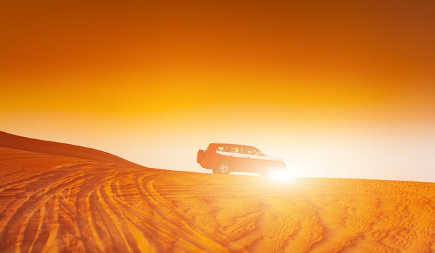 Offroad truck or suv riding dune in arabian desert at sunset. Offroad has been modified to be unrecognized.