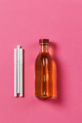 Three white cigarettes, bottle with alcohol cognac, whiskey on pink rose background. Health, choice, healthy lifestyle concept. Copy space for advertisement. With place for text.