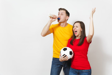 Fun crazy cheerful young couple, woman, man, football fans in yellow and red uniform cheer up support team with pipe soccer ball isolated on white background. Sport, family leisure, lifestyle concept.