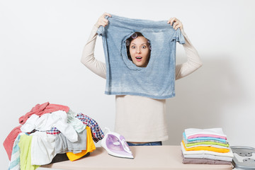 Smiling housewife, curlers on hair in light clothes holding burned shirt, looking through hole made...
