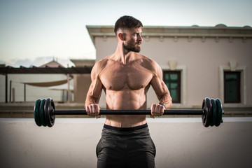 Fototapeta premium Shirtless muscular bearded man doing exercises with barbell outdoors.