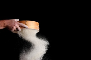 men's hands are sifting flour through a sieve on black background - obrazy, fototapety, plakaty