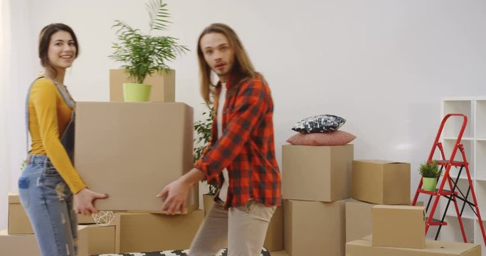 Young caucasian man and woman relocating home stuff and boxes by the living room while moving in together. Indoors