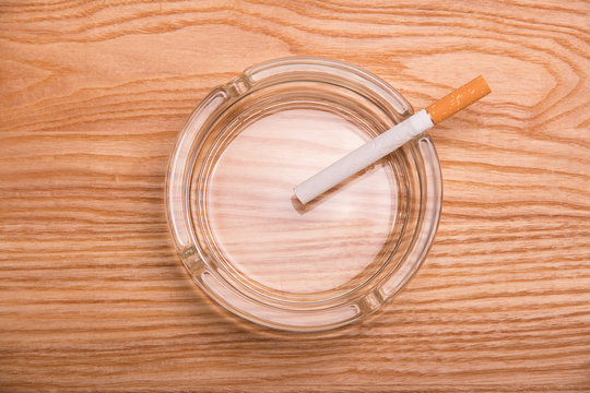 Cigarette with filter lies in an ashtray, on wooden surface