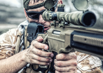 Private military contractor PMC sniper in baseball cap with assault rifle in the rocks