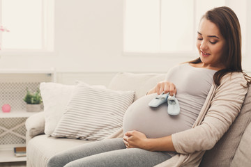 Pregnant woman holding tiny shoes near belly