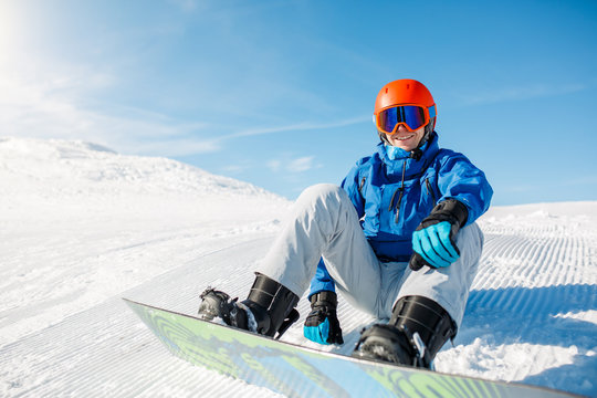 Photo of sports man wearing blue jacket, helmet with snowboard sitting on snowy slope
