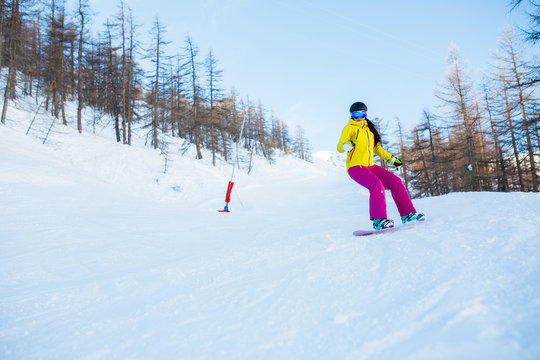Picture of athlete woman wearing helmet and mask snowboarding from snowy slope with trees