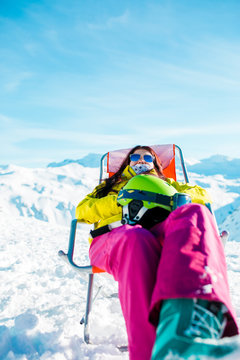 Pictures of sporty woman with helmet resting on chair in winter resort