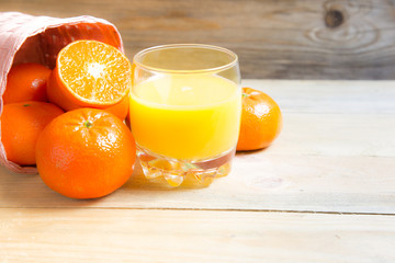 Fresh oranges in basket with a glass of fresh orange juice on wooden background.