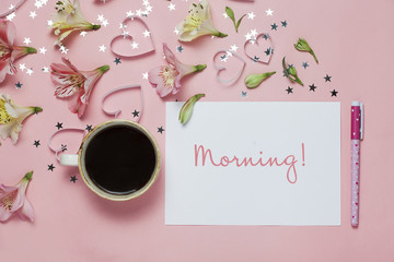 Cup of coffe and spring greeting with a pen, flower composition and word Morning on pink background. top view, flat lay