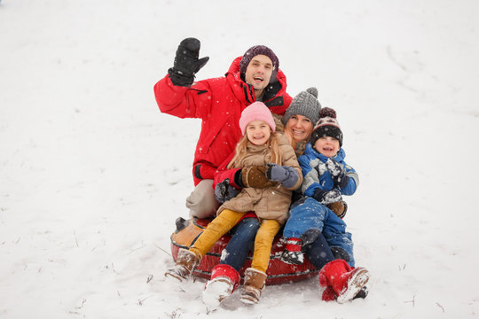 Photo of happy parents with daughter and son sitting on tubing in winter