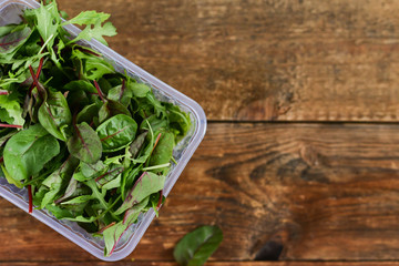 Fresh Greens Salad In a Plastic Box on wooden background: Salad Mix, Arugula, chard, Misun. The Concept Of Fast And Healthy Food, Organic Food, Vegetarianism.