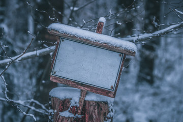 Empty, snowy, frozen white sign standing on a wooden pole at winter - no text, lots of copy space