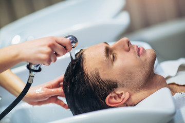 Hairdresser washing hair to her handsome client. Barber at work. Man at barbershop.