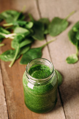 Green spinach juice jar on a rustic wooden table and spoon