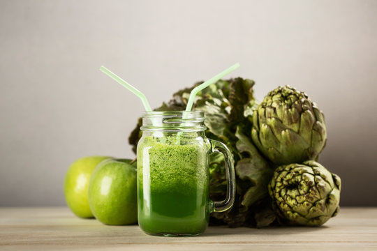 Green detox juice jar with green vegetables with two straws and vegetables in background.