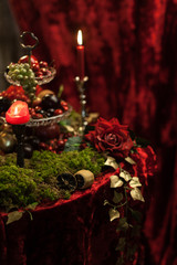 dark still life in red tones with candles, moss and roses