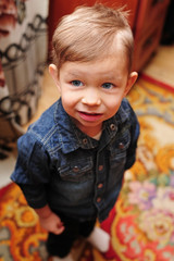 A cute little boy in a jeansy shirt stands and looks at the camera. Top view