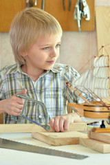 Fototapeta na wymiar boy with model of ship and handsaw