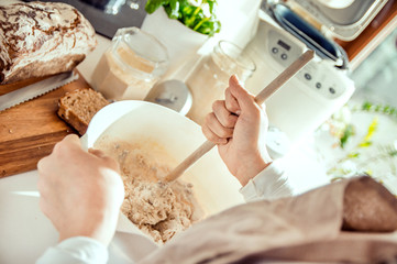 Fototapeta na wymiar woman mixing ingredients for home healthy bread. Photo taken in the light of natural sun and studio lamps. It contains delicate artistic noise and a vintage color grading