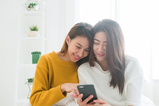 Beautiful young asian women LGBT lesbian happy couple sitting on bed hug and using phone together bedroom at home. LGBT lesbian couple together indoors concept. Spending nice time at home.