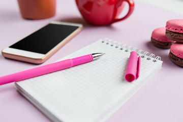 The side view on female desk. The phone and french macarons on trendy pink desk.