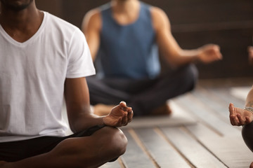 Young black man and a group of young sporty people practicing yoga lesson, sitting in Sukhasana...