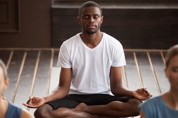 Young sporty black man practicing yoga lesson, sitting in Sukhasana exercise, Easy Seat pose with...
