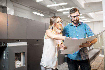 Young woman designer and print operator working together with paper print standing at the print...