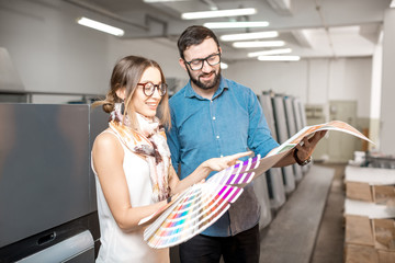 Young woman designer and print operator working together with color swatches standing at the print...