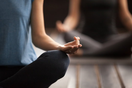 Sporty woman in blue t-shirt practicing yoga lesson, sitting in Sukhasana exercise, Easy Seat pose, working out, indoor close up focus on mudra gesture, studio