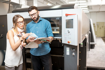 Young woman designer and print operator working together with color swatches standing at the print...