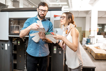 Young woman designer and print operator working together with color swatches standing at the print...